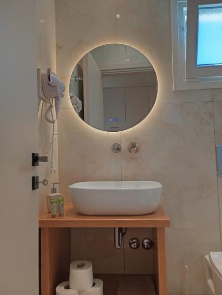 Baño moderno con lavabo sobre encimera de madera y espejo circular con luz LED en Elias & Vasili House