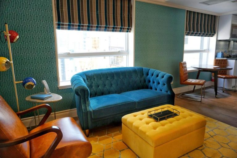 Salón moderno con sofá de terciopelo azul y puf amarillo en Hotel Madera Hollywood