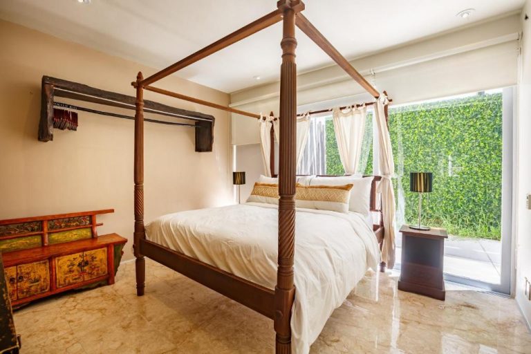 Habitación con cama de dosel de madera y vista al jardín verde en Magia Beachside Condo
