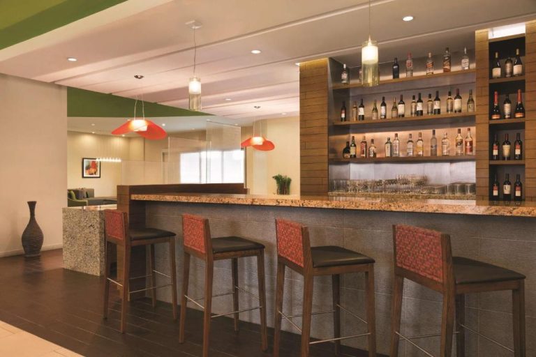 Bar con taburetes y estantes de licores del Hyatt Place San José Pinares en Costa Rica