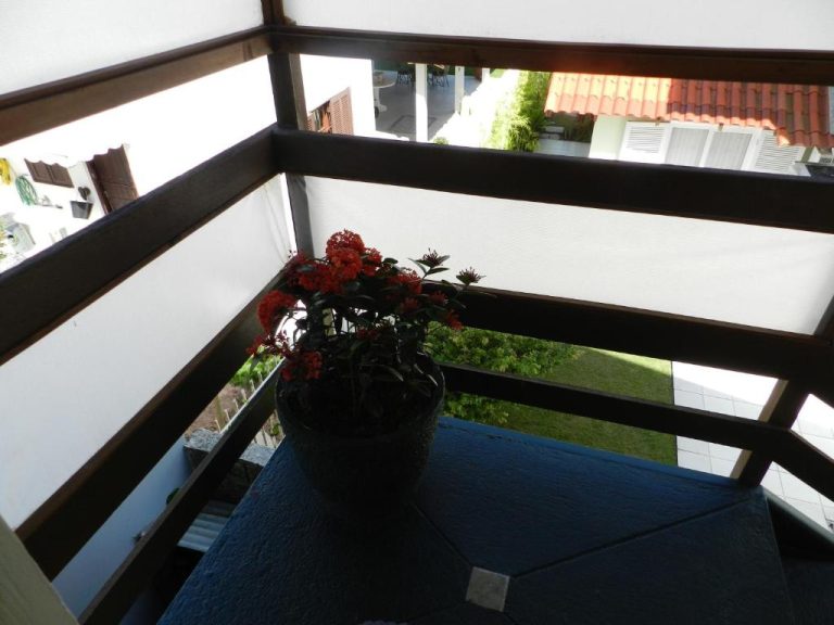 Balcón con maceta de flores rojas y vistas al jardín en Residencial Pontal do Jurerê