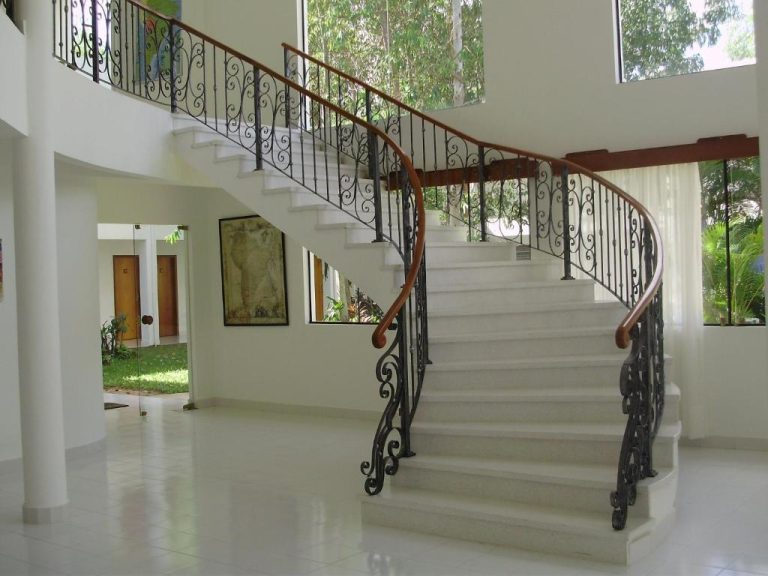 Elegante escalera curva de mármol blanco con barandilla de hierro forjado en el Hotel Ruta Del Sol
