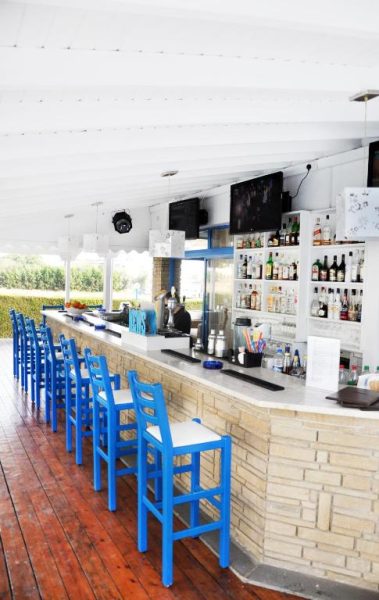 Bar terraza exterior con taburetes azules y barra de piedra en el Tasmaria Aparthotel