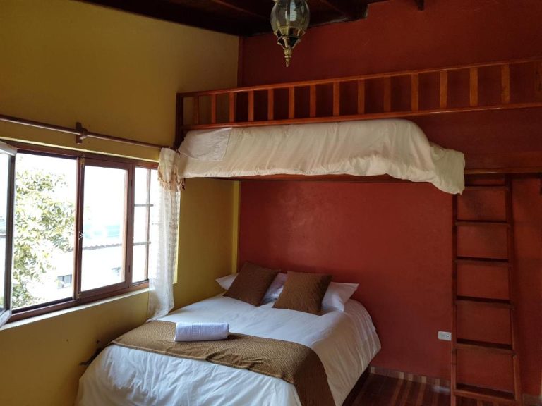 Habitación con cama doble y litera de madera en Hotel Fuentes del Volcán, decoración rústica en tonos rojos