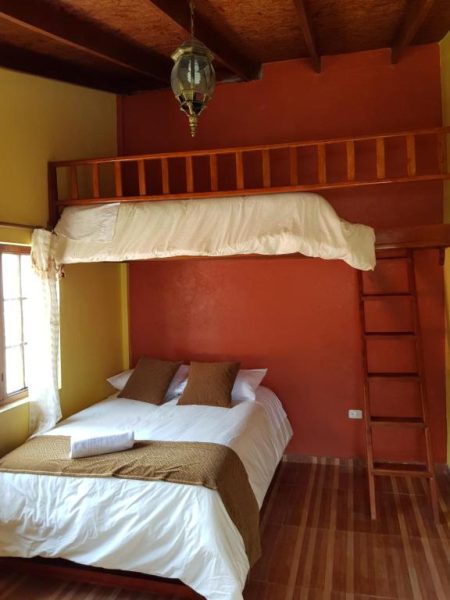 Habitación con cama doble y litera de madera en Hotel Fuentes del Volcán, decoración rústica en tonos rojos