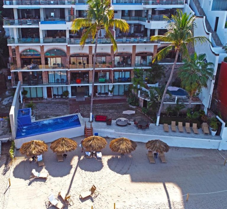 Vista aérea de la piscina y área de playa con palapas del Vallarta Shores Beach Hotel en Puerto Vallarta