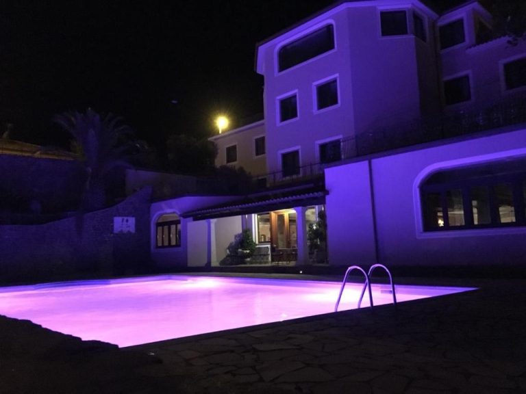 Piscina exterior iluminada en violeta por la noche en el Hotel Le Tre Rose con vistas a la villa