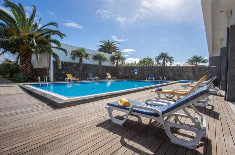 Piscina exterior con tumbonas y terraza de madera rodeada de palmeras en el Antillia Hotel
