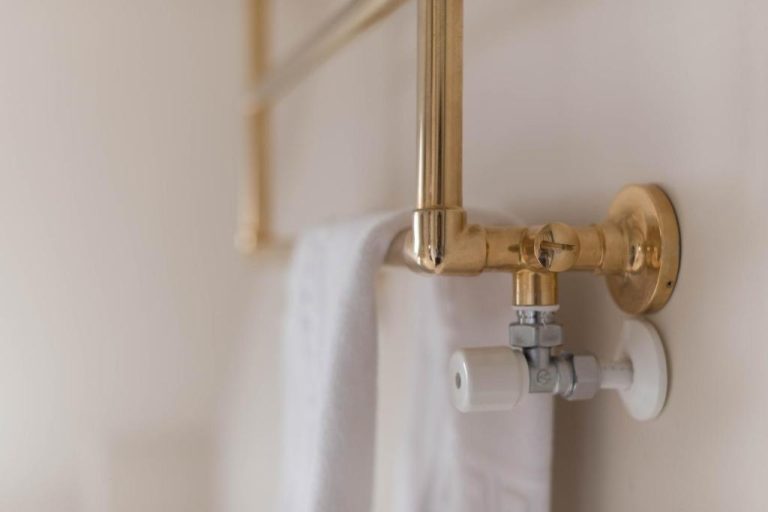 Toallero dorado con válvula de radiador y toalla blanca en el baño del Hotel Alquimista Montevideo