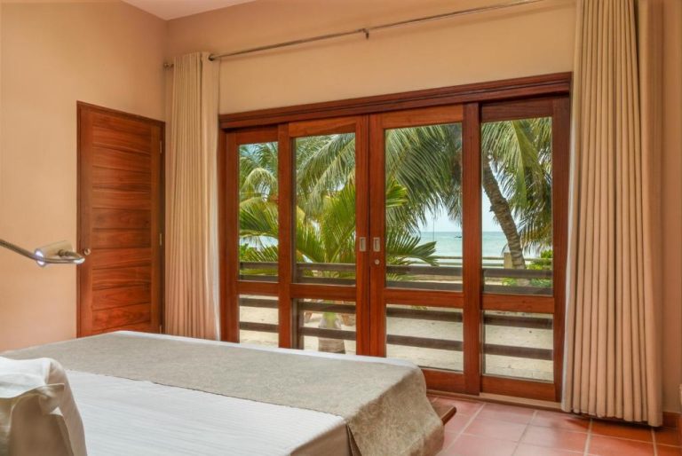 Habitación con cama doble y puertas de madera con vistas al mar y palmeras en Hotel Fleur de Sel
