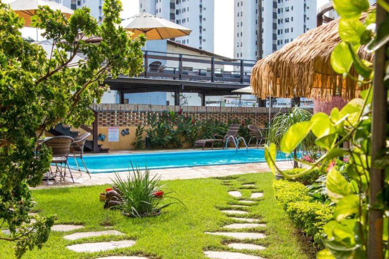 Piscina exterior rodeada de jardín tropical con palapa en Pousada da Terra