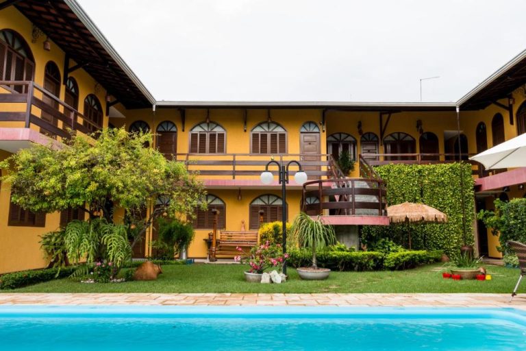 Piscina exterior con jardín tropical y fachada amarilla de la Pousada da Terra