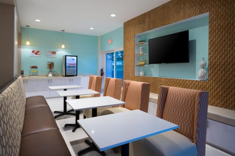 Salón de desayunos moderno con mesas blancas y TV del Holiday Inn Express & Suites Nassau
