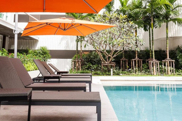 Piscina exterior con tumbonas y sombrillas naranjas en The Base Downtown Phuket Town