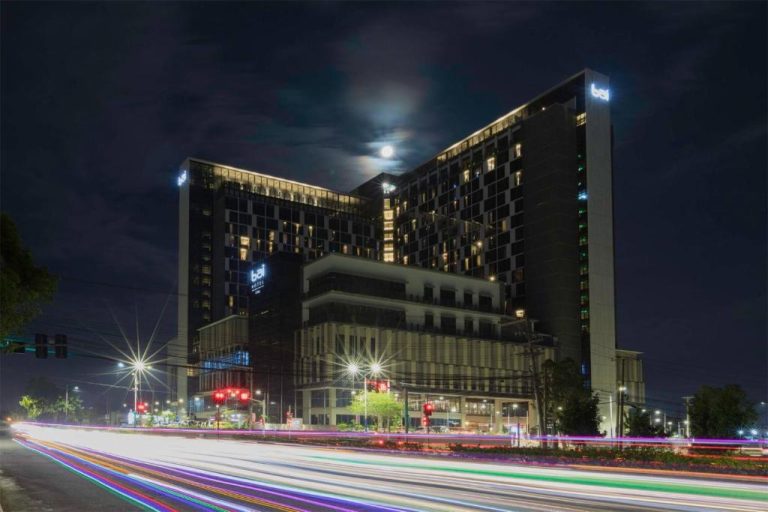 Vista nocturna de la fachada exterior del Bai Hotel Cebu con luces de tráfico y luna llena
