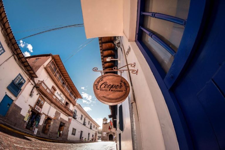 Fachada y letrero de madera del Cooper Hotel Boutique en una calle empedrada del centro histórico de Cusco