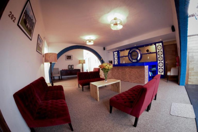 Lobby con sofás rojos y recepción iluminada del Cooper Hotel Boutique con arco decorativo azul