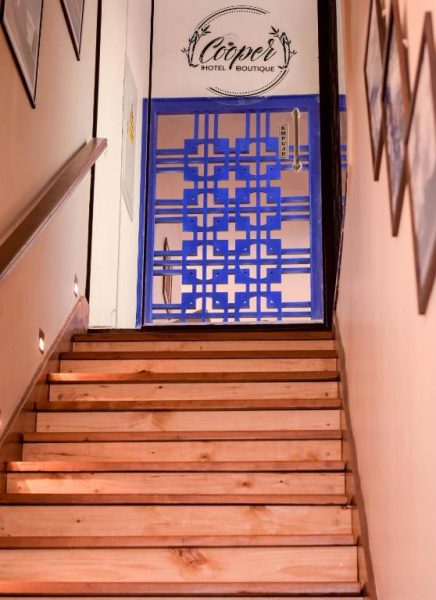Escaleras de madera y puerta decorativa azul en la entrada del Cooper Hotel Boutique