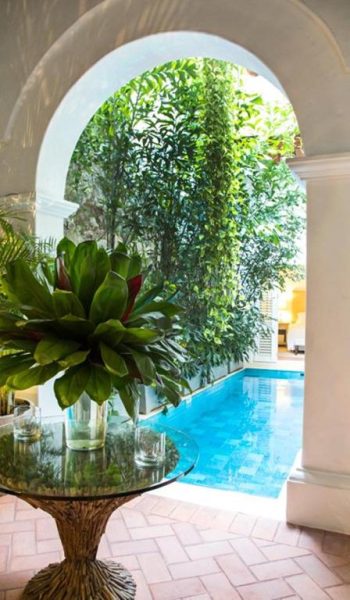 Piscina interior rodeada de vegetación tropical en Hotel Casa Don Sancho by Mustique, vista desde arco colonial