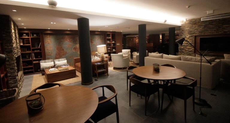 Salón lounge con biblioteca y mesas de madera en Cottage Puerto Buceo, ambiente cálido y elegante
