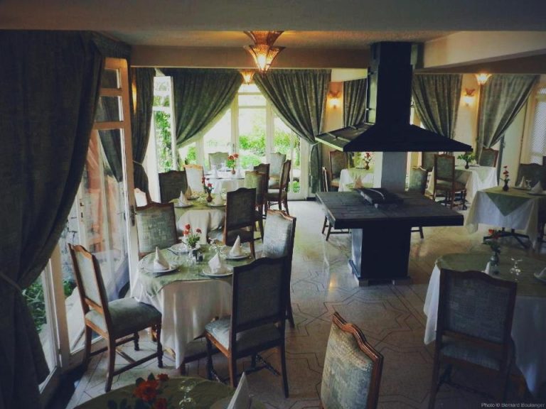 Elegante restaurante del Auberge des Cascades Imouzzer con mesas vestidas y chimenea central en Paradise Valley