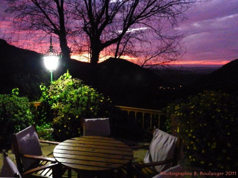 Terraza exterior con mesa y sillas de madera al atardecer en Auberge des Cascades Imouzzer Paradise Valley