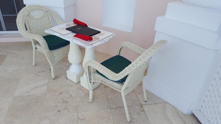 Mesa y sillas de mimbre blanco con cojines verdes en la terraza del Ocean West Boutique Hotel