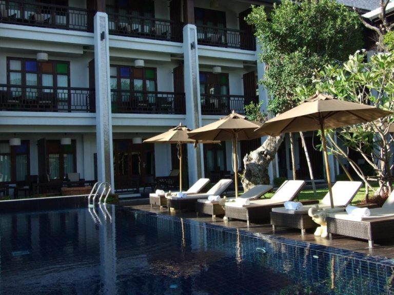 Piscina exterior con tumbonas y sombrillas del De Lanna Hotel rodeada de jardín tropical