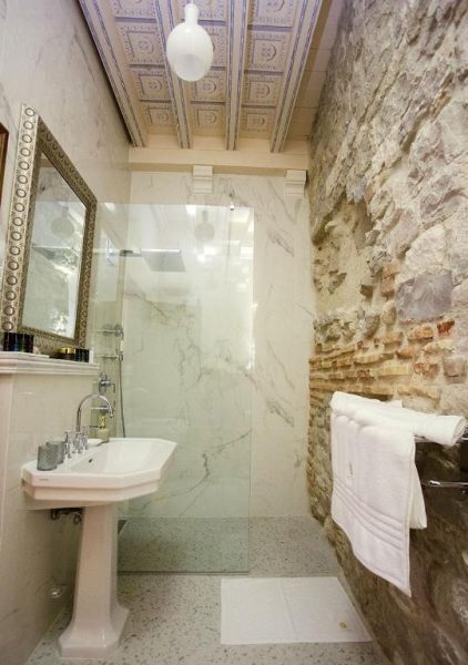 Baño con pared de piedra y ducha de mármol con techo decorativo en Heritage Hotel Cardo