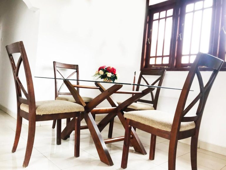 Comedor con mesa de cristal y sillas de madera en 360 Beach Residence con flores decorativas