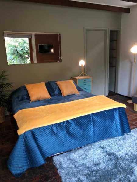 Habitación doble con cama azul y cojines dorados en Rent Apart Las Condes, con televisor y closet