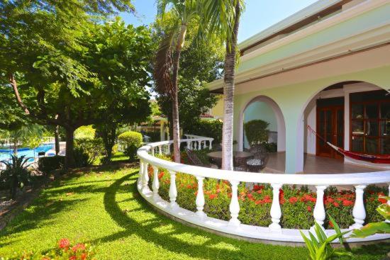 Terraza con balaustrada blanca, jardín tropical y piscina exterior en Villa del Sueño