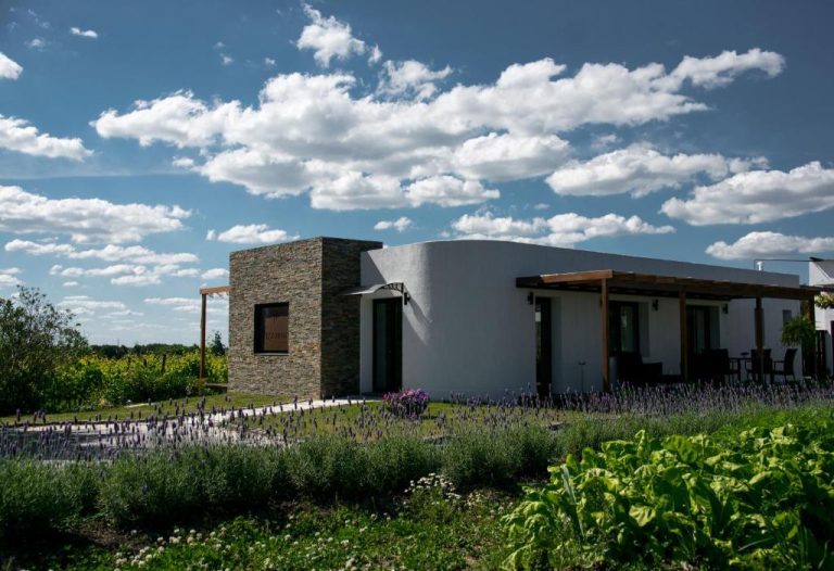 Fachada exterior del Pizzorno Lodge & Wine rodeada de campos de lavanda y jardines bajo cielo azul