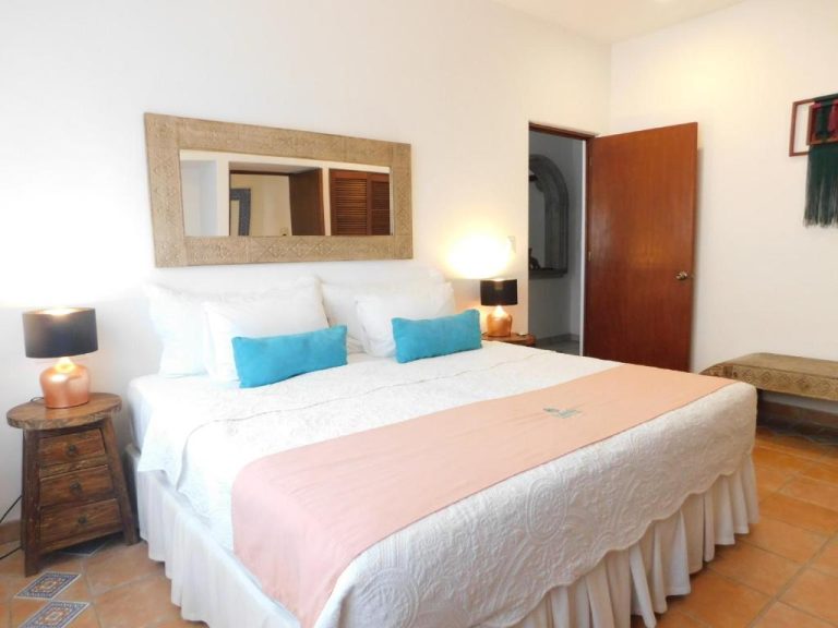 Habitación con cama king size y almohadas azules en Fabiola Condo Hotel, decoración colonial mexicana