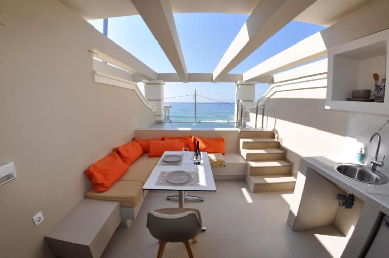 Terraza con sofá naranja, mesa de comedor y piscina con vistas al mar en Agios Gordios Beach Resort