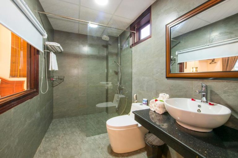 Baño moderno con ducha de cristal, lavabo y espejo en Bonsai Villa Hoi An
