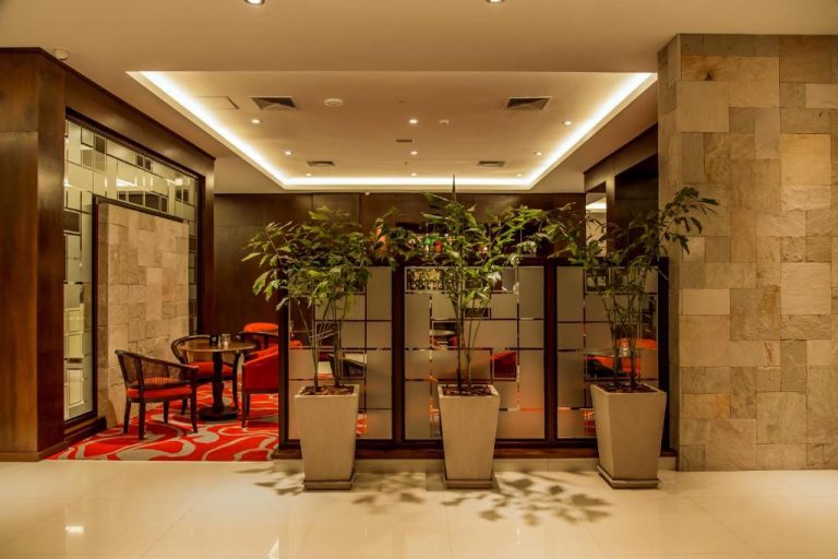 Elegante lobby del Carnaval Hotel Casino con plantas decorativas, espejos y zona lounge con sillones rojos