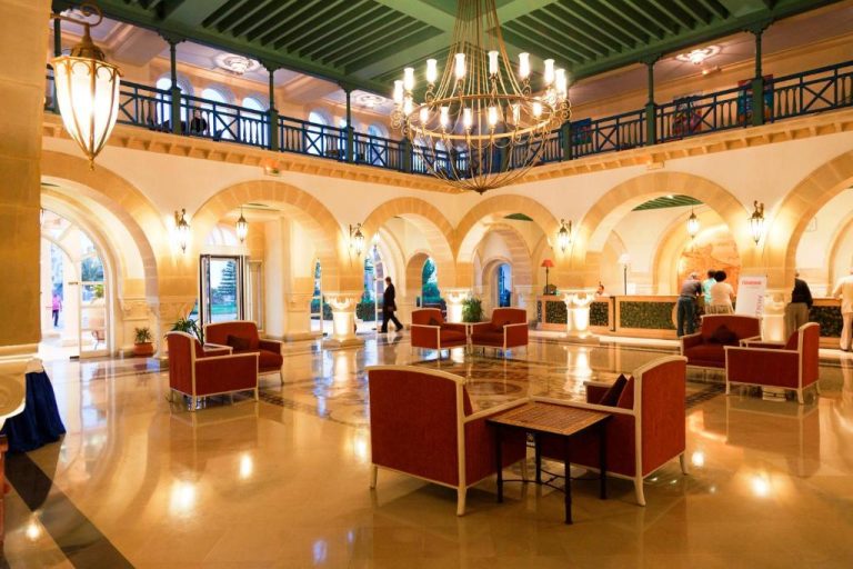 Lujoso lobby con arcos y araña de luces del Regency Hotel & Spa con sillones rojos