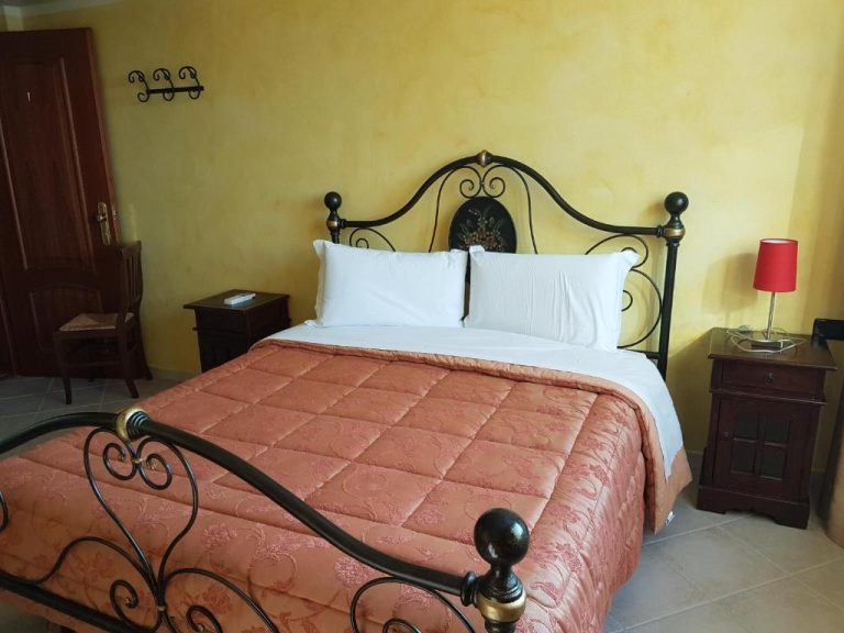 Habitación doble con cama matrimonial de hierro forjado y colcha roja en Hotel Le Tre Rose