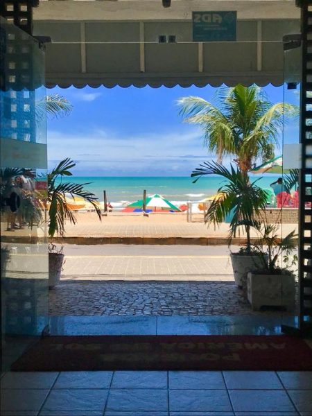 Vista a la playa desde la entrada de Pousada America do Sol con palmeras y sombrillas de colores