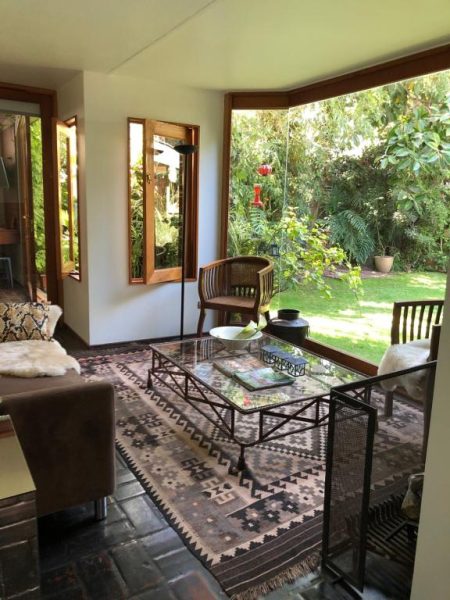 Sala de estar con mesa de cristal y terraza abierta al jardín verde en Rent Apart Las Condes