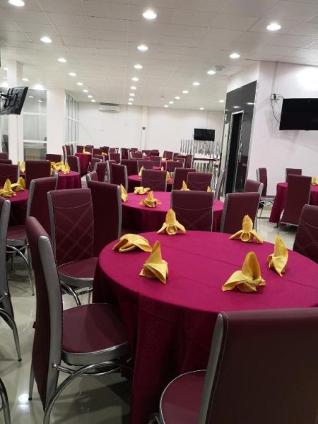 Salón de eventos con mesas redondas y manteles granate en Manarat Manah Hotel Apartments
