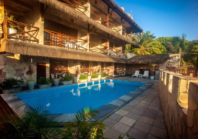 Piscina exterior con tumbonas y balcones de madera del Castelo Beach Hotel rodeada de palmeras