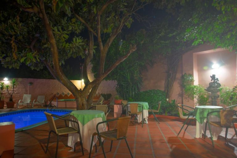 Terraza exterior con mesas y sillas junto a la piscina iluminada de noche en Posada del Frayle Bentos