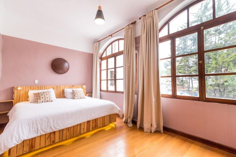 Habitación doble con cama de madera y grandes ventanas en Viajero Quito Hostel