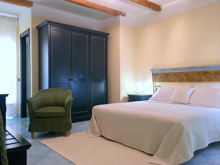 Habitación doble con cama matrimonial, cabecero tallado y armario oscuro en Hotel Su Lithu