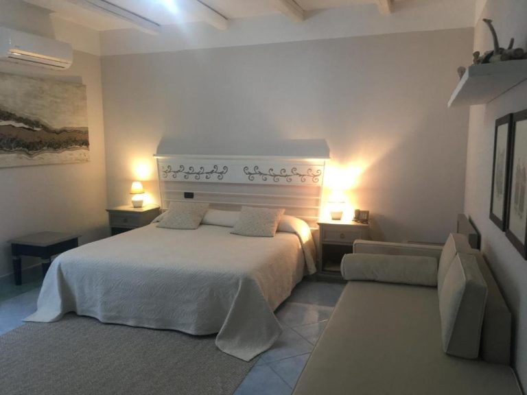 Habitación doble con cabecero blanco decorado y lámparas de mesita en Hotel Su Lithu