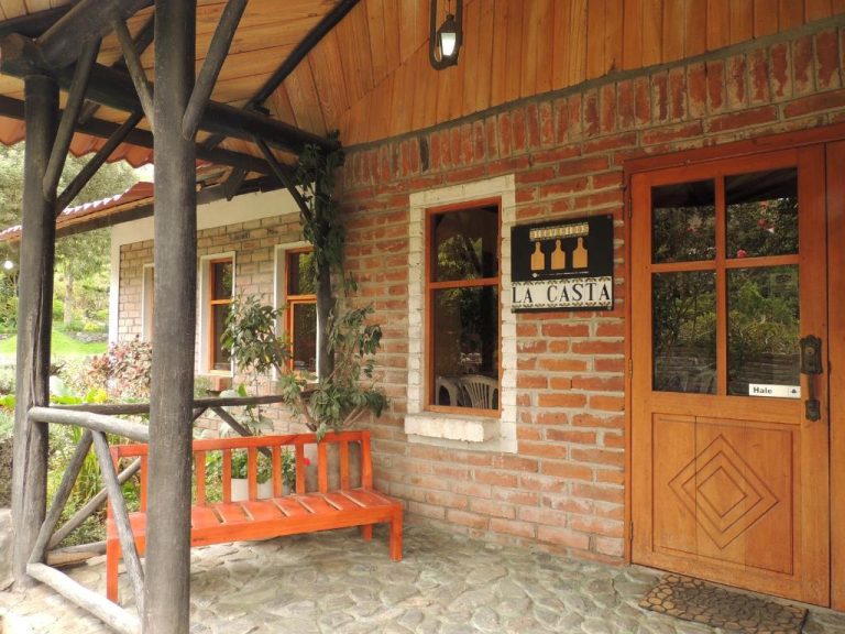 Fachada exterior de La Casta con entrada de madera, banco rojo y paredes de ladrillo rústico
