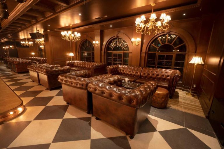 Elegante salón con sofás Chesterfield de cuero marrón y candelabros dorados en Jazz Hotel Penang