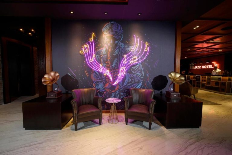 Lobby del Jazz Hotel Penang con mural de músico de jazz iluminado en neón y gramófonos decorativos